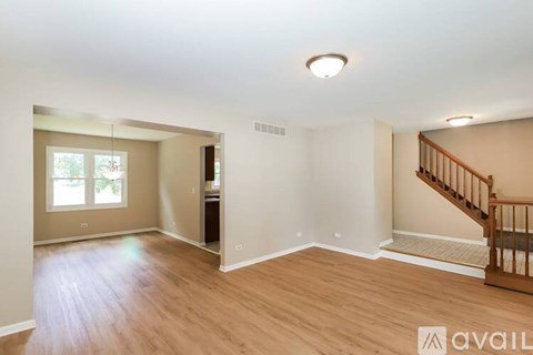 A spacious room with wooden floors and a staircase on the right side.