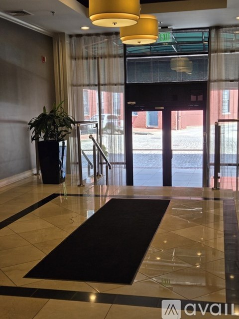 A hallway with a black and white rug, a potted plant, and a yellow light fixture.