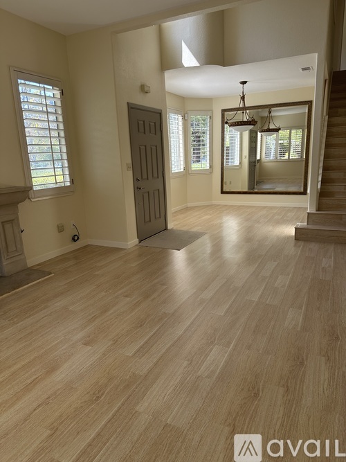 A spacious room with wooden flooring and a staircase on the right side.