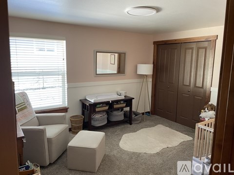 A room with a white ceiling, a brown door, a white chair, a white ottoman, a white table, and a white rug.