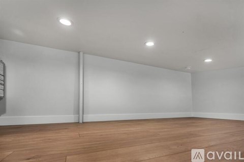 A spacious room with wooden flooring and white walls.
