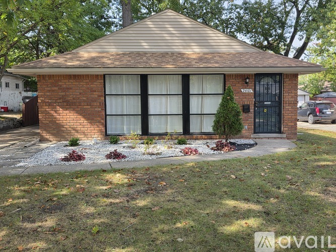 A small house with a black door and windows is surrounded by a gravel area and some plants.