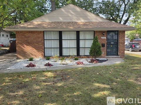 A small house with a black door and windows is surrounded by a gravel area and some plants.