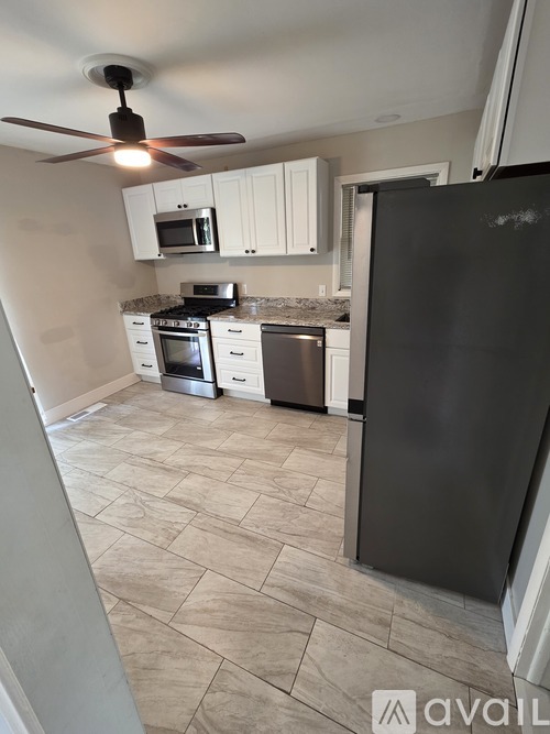 A kitchen with a black refrigerator, white cabinets, and a ceiling fan.