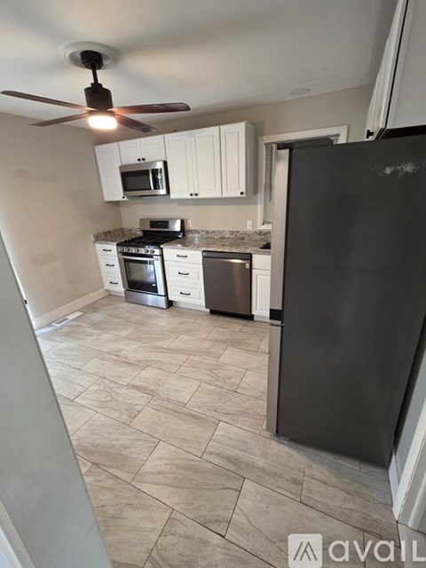 A kitchen with a black refrigerator, white cabinets, and a ceiling fan.