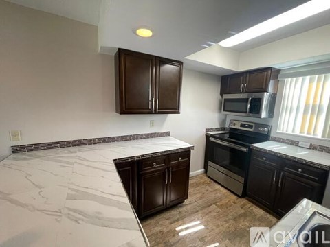 A kitchen with dark brown cabinets and a marble countertop.