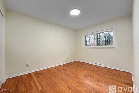 A room with wooden flooring and a window showing trees outside.