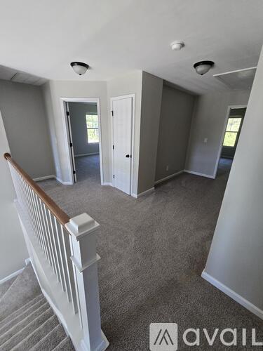 A living room with a carpeted floor and a staircase with white railings.