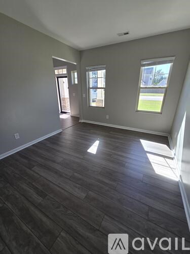 A spacious room with wooden flooring and large windows.