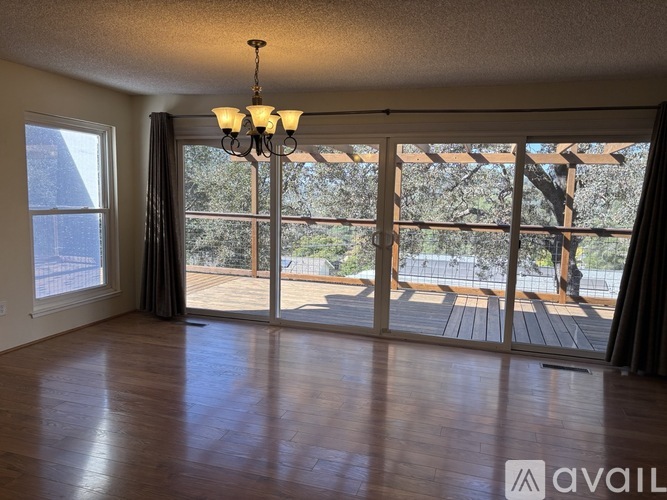 A room with wooden floors and a chandelier with a view of a deck outside the window.