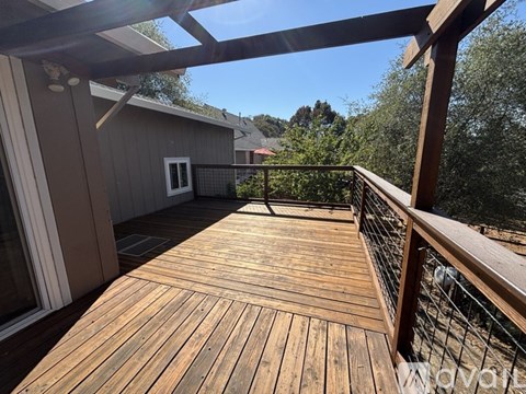 A wooden deck with a metal railing and a view of a house and trees.