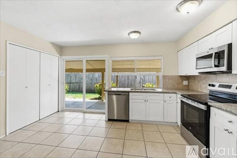 A kitchen with white cabinets and appliances, a tiled floor, and a sliding glass door leading to a backyard.