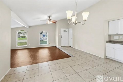 A room with a brown floor and white walls, with a chandelier and a ceiling fan.