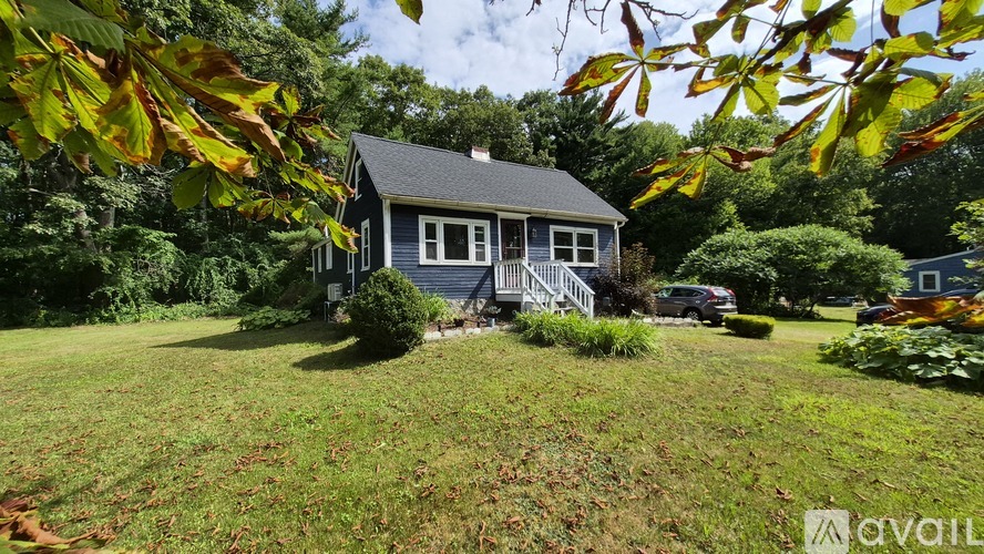 A house with a blue roof and white trim is surrounded by greenery.