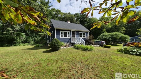 A house with a blue roof and white trim is surrounded by greenery.