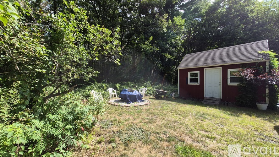 A small red shed sits in a grassy area with trees and bushes around it.