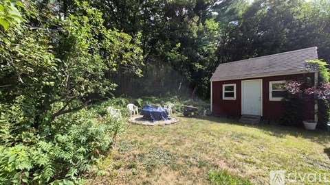 A small red shed sits in a grassy area with trees and bushes around it.
