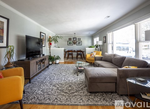 A living room with a grey sofa, a yellow chair, a black television and a rug.