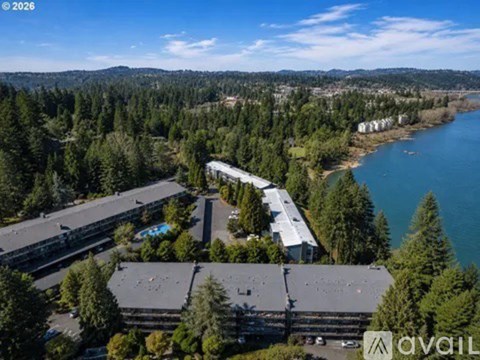 An aerial view of a large building complex surrounded by trees with a body of water in the background.
