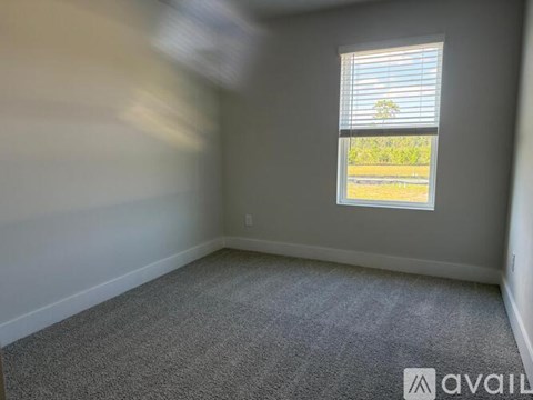 A room with a carpeted floor and a window showing a view of trees and a grassy area outside.