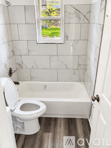 A white toilet in a bathroom with a marble wall and a window.