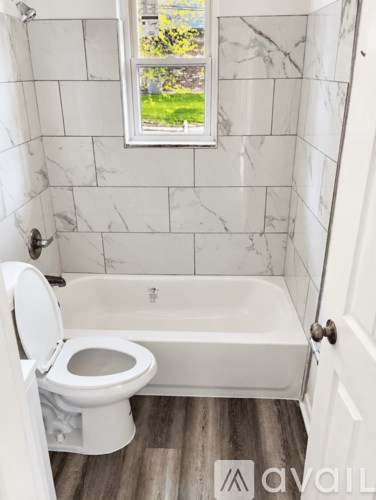 A white toilet in a bathroom with a marble wall and a window.