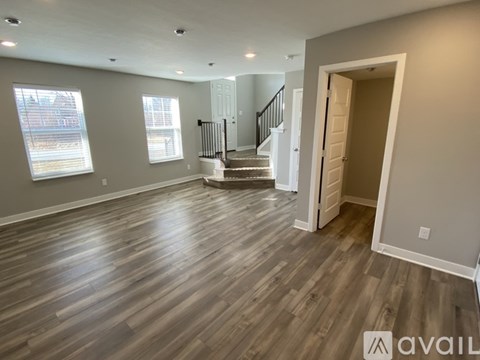 A spacious room with wooden flooring and a staircase in the background.