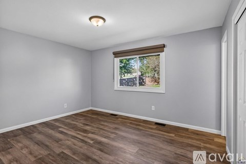 A room with wooden flooring and a window showing a view of a tree and a building.