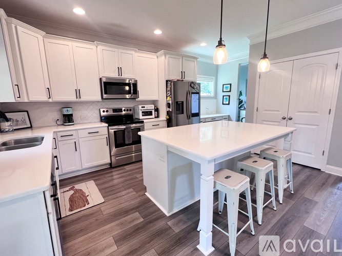 A kitchen with white cabinets and a large island with four stools.