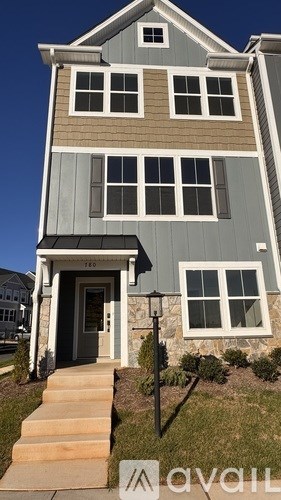 A two-story house with a grey and beige exterior and a stone pillar on the front porch.