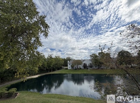 A serene landscape with a lake, trees, and a house in the distance.