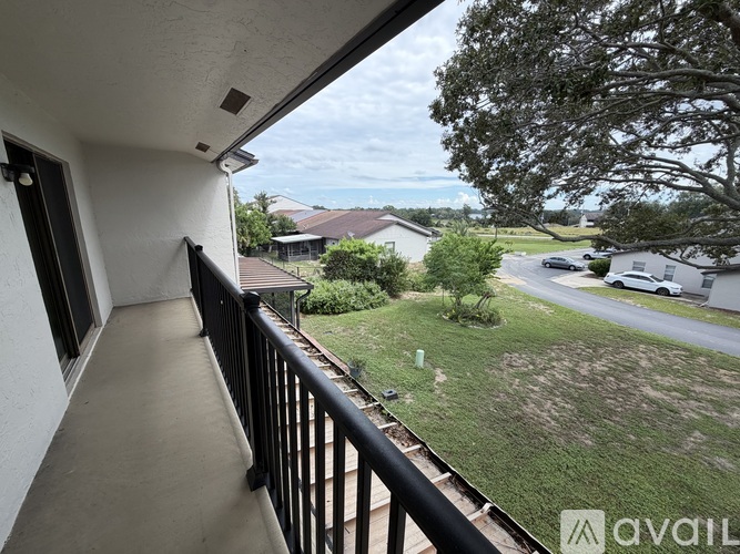 A balcony overlooks a grassy area with a house and cars in the distance.