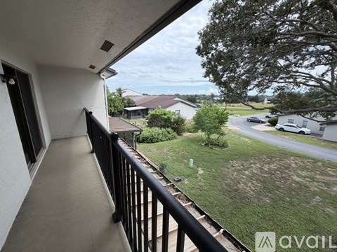 A balcony overlooks a grassy area with a house and cars in the distance.
