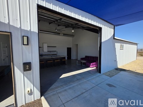 A white building with a garage door open to a room with a couch and a fan.