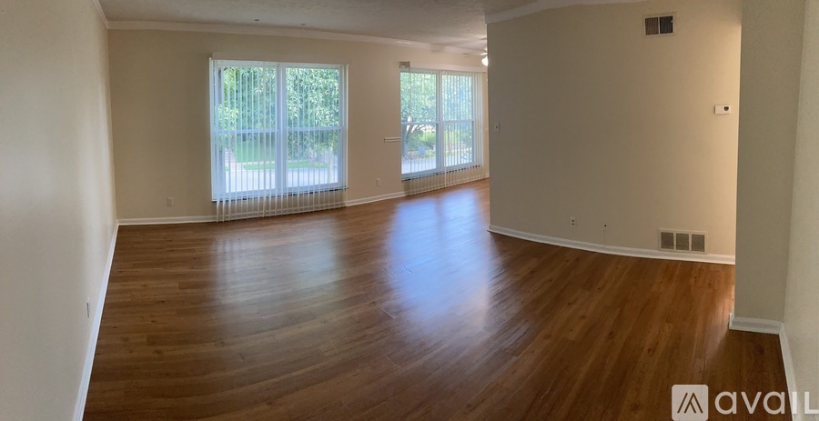 A spacious room with wooden floors and a large window with blinds.