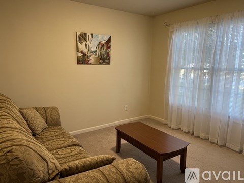 A living room with a brown sofa and a painting on the wall.