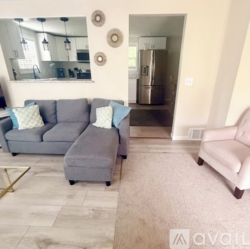A living room with a grey couch and ottoman, a pink chair, and a kitchen in the background.