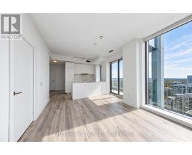 A spacious, well-lit room with wooden floors and large windows overlooking a cityscape.