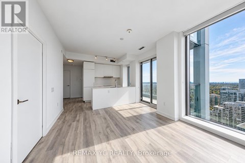 A spacious, well-lit room with wooden floors and large windows overlooking a cityscape.