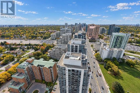 A cityscape with a mix of modern and older buildings, a clear sky, and a road with moving vehicles.