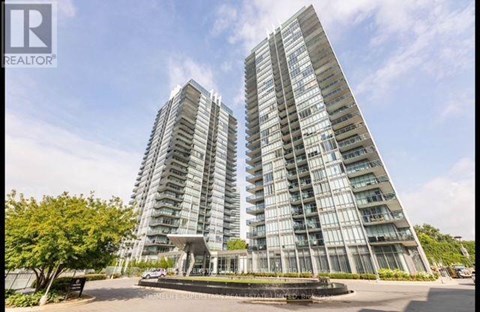 A tall residential building with a glass facade stands under a clear blue sky.