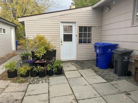 A small garden with a white door and a blue trash bin.