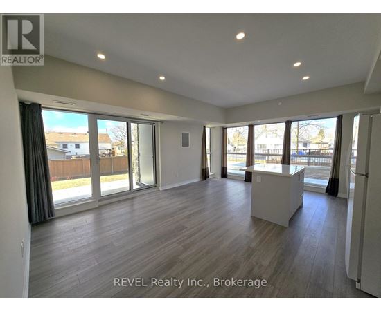 A spacious room with wooden flooring and large windows.