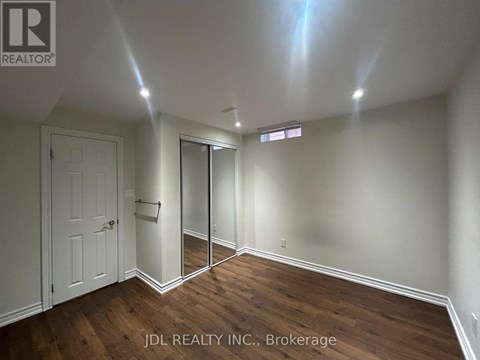 A room with wooden floors and white walls, with a door and a mirror on the wall.