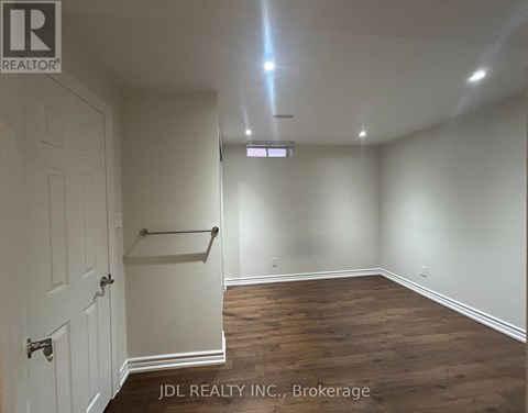 A room with wooden flooring and white walls, with a door on the left and a shelf on the right.