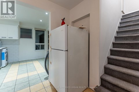 A kitchen with a white fridge and a staircase.