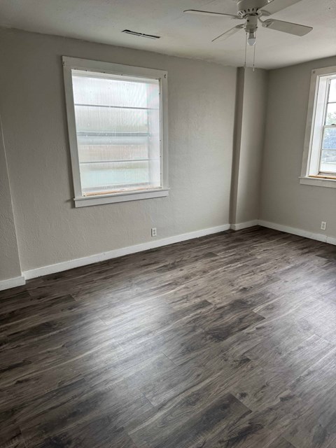 A room with a ceiling fan and two windows.