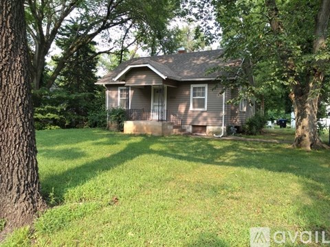 A house with a brown roof and a porch is surrounded by trees.