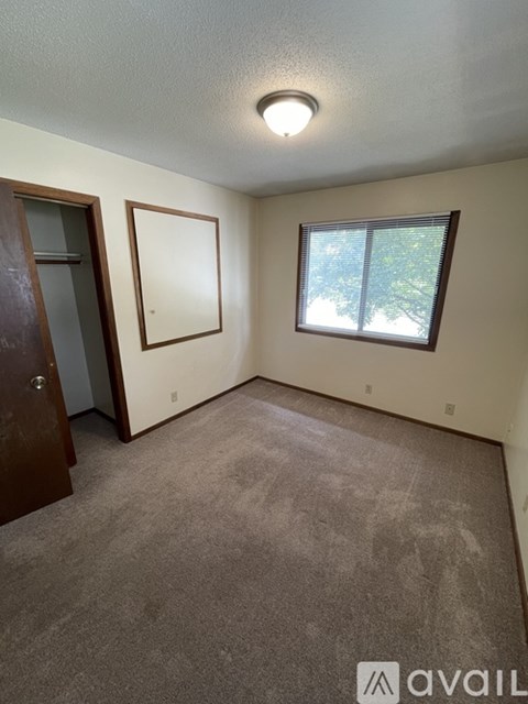 A room with a carpeted floor, a window with a view of trees, and a door.
