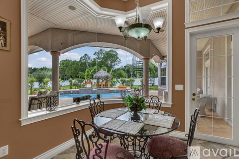 A dining room with a glass table and chairs, a chandelier, and a view of a pool and trees through the windows.